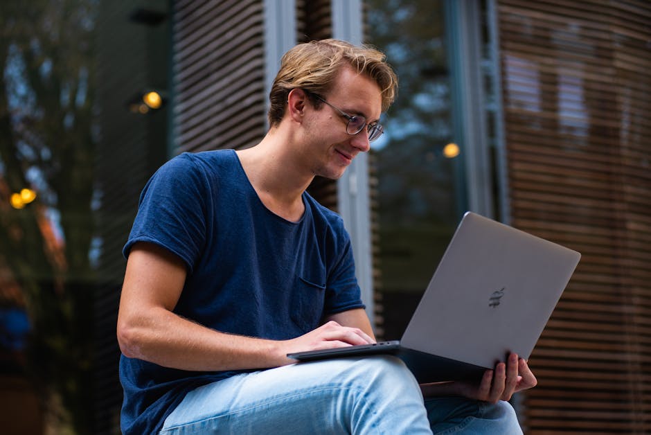 A young man sitting outdoors working on a laptop